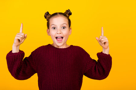 Portrait of astonished smart small girl point fingers bright great idea isolated on yellow color backgroundの写真素材
