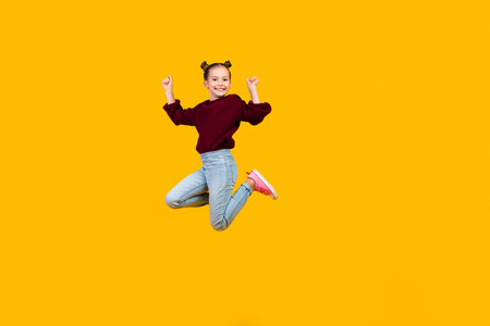 Full body portrait of overjoyed small schoolkid jumping raise fists empty space isolated on yellow color backgroundの写真素材