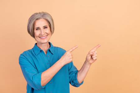 Portrait of good mood person with white gray hairdo wear blue shirt indicatign at offer empty space isolated on pastel color backgroundの写真素材