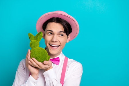 Photo portrait of handsome young guy hold grass easter bunny look empty space wear trendy pink...