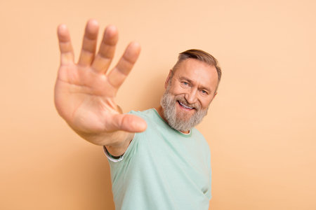 Photo of glad cheerful man waving hands showing fingers high five symbol isolated on beige color backgroundの写真素材