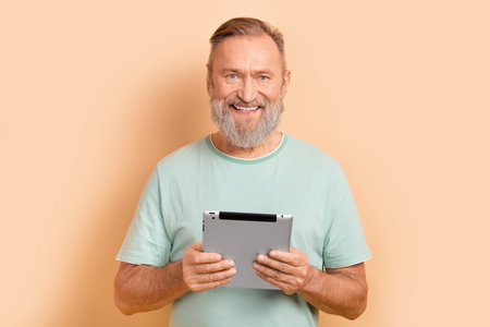 Portrait of intelligent satisfied retired man with beard wear stylish t-shirt hold tablet read ebook...