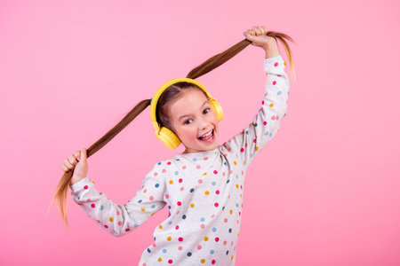 Photo of funky positive small girl holding tails hairstyle wear stylish sweatshirt in headphones isolated on pink color backgroundの写真素材