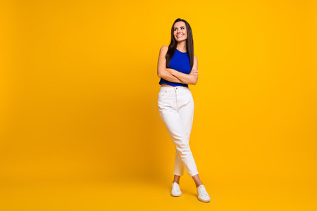 Full length photo of dreamy sweet woman wear blue top arms crossed looking empty space isolated yellow color backgroundの写真素材