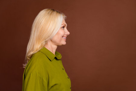 Side profile photo of good mood adorable woman with stylish hairdo look at promo empty space isolated on dark brown color backgroundの写真素材