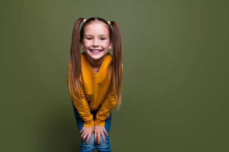 Portrait of adorable small kid with tails dressed yellow sweatshirt hands on knees smiling to you...