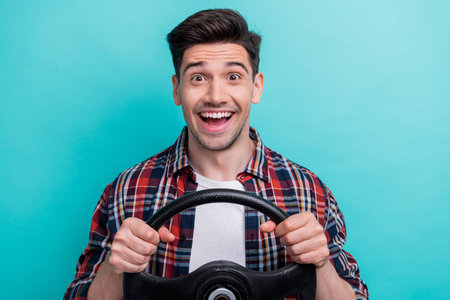 Photo of excited cheerful man dressed plaid shirt smiling driving auto isolated turquoise color backgroundの写真素材