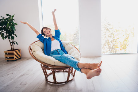 Photo of cheerful cute adorable girl rejoicing free time vacation sitting in soft chair cozy living roomの写真素材