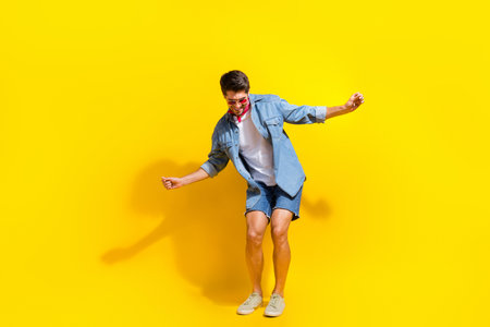 Full size photo of funky cheerful guy wear jeans jacket shorts in sunglass dancing near empty space isolated on yellow color backgroundの写真素材