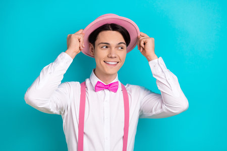 Photo of attractive young man look empty space touch headwear dressed stylish pink clothes isolated on aquamarine color backgroundの写真素材