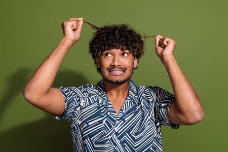 Photo of impressed unhappy guy wear print shirt dislike hairdo curls isolated khaki color backgroundの写真素材
