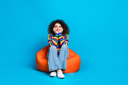 Full length photo of lovely young lady sit cute look up empty space dressed stylish rainbow print garment isolated on blue color backgroundの写真素材
