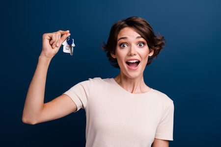 Photo portrait of attractive young woman real estate shopping hold key wear trendy white clothes isolated on dark blue color backgroundの写真素材