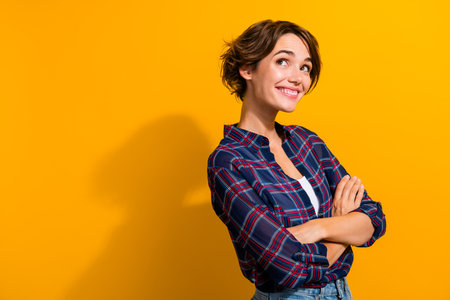 Photo of dreamy woman with short hairdo dressed plaid shirt palms folded look at offer empty space isolated on yellow color backgroundの写真素材