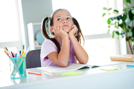 Photo of unsatisfied minded schoolkid sit chair hands touch cheeks look curious away ponder flat...