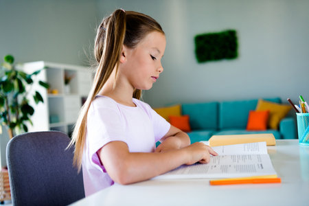 Profile photo of charming clever girl sit chair read opened book prepare test exam courses house indoorsの写真素材
