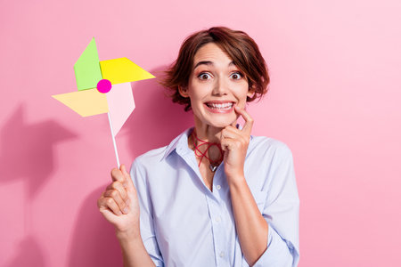 Photo of creative cheerful lady finger touch lips toothy smile hold windmill spinner isolated on pink color backgroundの写真素材