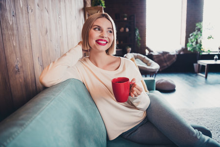 Portrait of adorable creative person sit sofa hold hot chocolate mug brainstorming fantasize apartment indoorsの写真素材