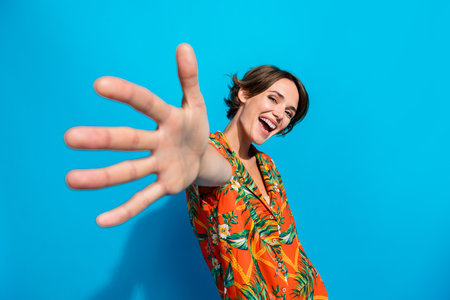 Portrait of gorgeous positive girl toothy smile raise opened arm palm camera you invite isolated on blue color backgroundの写真素材