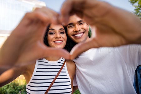 Photo of attractive lovely cheerful couple wife and husband showing in camera heart shape romantic date outsideの写真素材