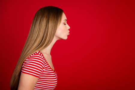 Photo of positive dreamy girl wear striped top closed eyes kissing empty space isolated red color backgroundの写真素材