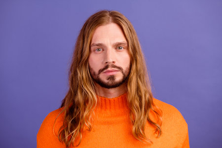 Portrait photo of young hippie guy in orange stylish sweater confident long hair blond with beard isolated on violet color backgroundの写真素材