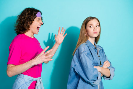 Photo of couple teenagers furious conflict boyfriend offense his girlfriend folded hands looking him isolated on cyan color backgroundの写真素材