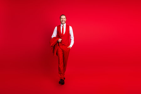 Full body photo of attractive young man confident walking hold jacket wear trendy classic clothes isolated on red color backgroundの写真素材