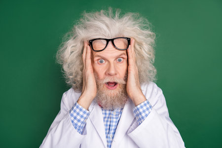 Photo of shocked crazy amazed surprised scientist with messy hair having problem isolated on green color backgroundの写真素材