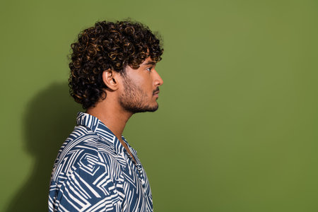 Side photo of young indian guy wavy hair model with stubble looking empty space likes barbershop ad isolated on khaki color backgroundの写真素材