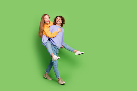 Full body profile photo of two positive idyllic partners piggyback walk empty space isolated on green color backgroundの写真素材