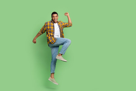 Full size portrait of overjoyed person jump raise fists achievement empty space isolated on green...