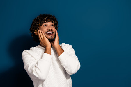 Photo of young funny crazy guy in white jumper touch cheeks looking empty space staring impressed...