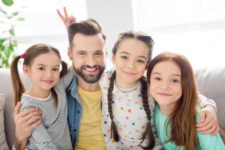 Photo of four people cheerful guy hugging adorable friendly girls fingers show horns head have fun home indoorsの写真素材