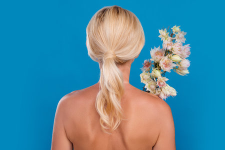 Photo of pretty shiny senior woman nude shoulders standing back holding bouquet isolated blue color...