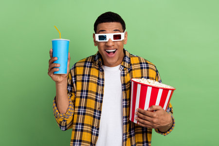 Photo of astonished man hold big popcorn bucket soda drink cup watch movie 3d glasses isolated on...