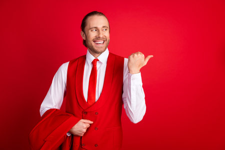 Photo portrait of attractive young man hold jacket point look empty space dressed stylish classic clothes isolated on red color backgroundの写真素材