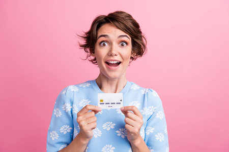 Portrait of astonished nice person open mouth arms hold plastic debit card isolated on pink color...