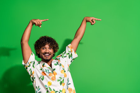 Photo of cool positive arabian man wear print shirt pointing two fingers empty space isolated green color backgroundの写真素材