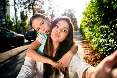 Portrait of two cute funny girls cuddle pouted lips kiss take selfie record video pastime sunshine outdoorsの写真素材