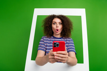 Portrait of speechless impressed person inside album set card stare hold smart phone isolated on green color backgroundの写真素材