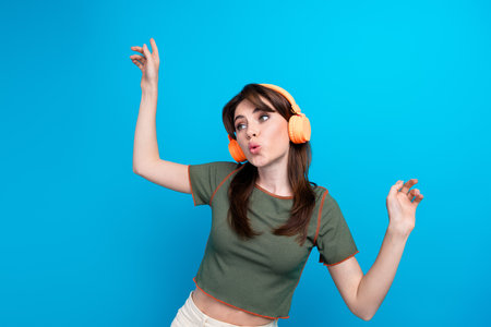 Photo of cute carefree person raise hands dance listen music headphones isolated on blue color...