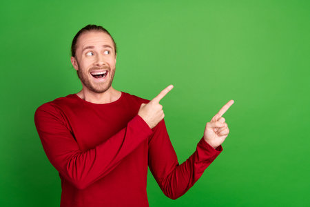 Portrait of ecstatic guy with long hair wear red shirt directing look at impressive offer empty...