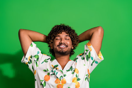 Photo of funky dreamy arabian man wear print shirt closed eyes arms behind head isolated green color backgroundの写真素材