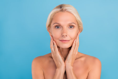 Photo of shiny pretty elderly lady naked shoulders arms touch cheekbones apply mask isolated blue color backgroundの写真素材
