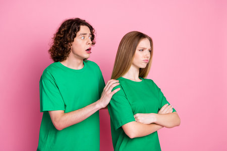Photo of teenagers couple wearing green t shirt boyfriend touching shoulders say sorry to offended girl isolated on pink color backgroundの写真素材