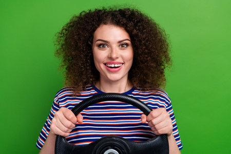 Portrait of cheerful nice girl toothy smile arms hold steering wheel isolated on green color...