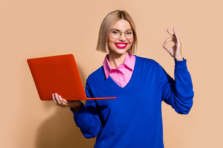 Photo of charming successful person hold laptop demonstrate okey symbol feedback isolated on beige color backgroundの写真素材