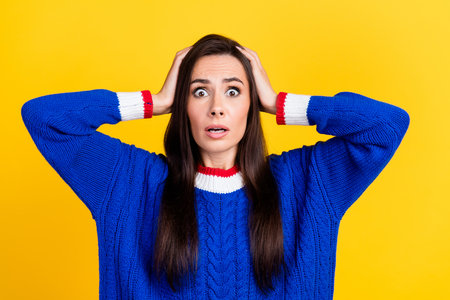 Portrait of funny hispanic woman wearing blue knit pullover hands touching head stressed staring...