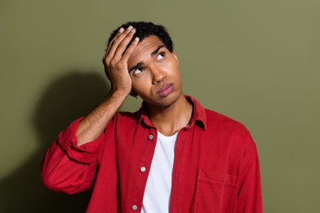 Photo of doubtful unsure man dressed red shirt arm head looking empty space isolated green color...